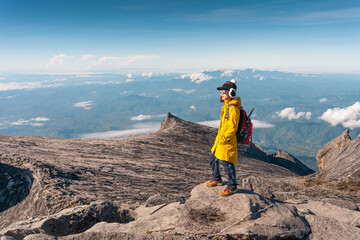 Young Asian woman trekker with backpack standing on top of Low's peak of Kinabalu mountain massif, Borneo island in Sabah state, Malaysia - obrazy, fototapety, plakaty