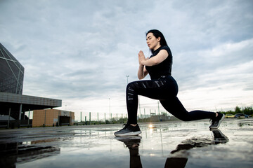 Fototapeta premium Bottom view, young sporty brunette is training outdoors. Woman makes lunges outdoors. Fitness, workout, sport concept