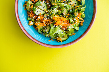 Vegetarian salad. Diet salad of fresh vegetables on a yellow background. Salad of fresh cucumbers, lettuce, carrots, green onions and sesame seeds.