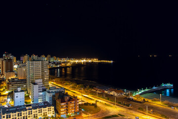 Fototapeta na wymiar Long exposure panoramic view of the quiet beach, the calm water, the empty streets and the illuminated harbor seen from a hotel room balcony on a clear dark night at coast city Punta Del Este, Uruguay