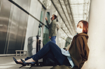 Young woman in medical mask sits near luggage in airport. Tortured by the flight, the woman dozes off before the next flight. Travel and coronavirus concept