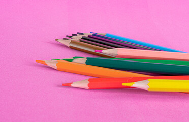 Multi-colored pencils are scattered on a bright pink background. School supplies. Foreground Defocus