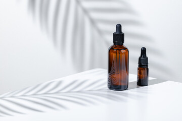 Creative photo of cosmetic bottle with pipette on a white background with shadow of tropical flower