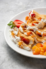 Crepe plate with fruit, berries, sour cream on concrete background. Dessert thin pancakes with strawberry and peach.