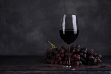 The red wine in the glass, along with a bottle of wine made from red grapes, is laid on a wooden...