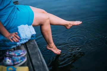 woman sitting on a wooden bridge near the water, dangled her legs and touches the surface of the water