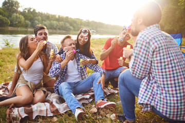 Fototapeta premium Young people make soap bubbles while sitting on the grass on in nature.