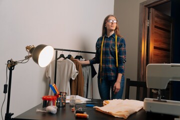 A brooding seamstress stands next to things. Tailor removes clothes on dress hangers
