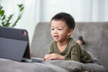 Asian boy with a cute face and good temper is looking and smiling at the camera in front of the tablet. While talking to friends via video call.