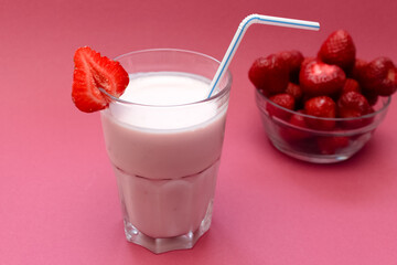 Strawberry smoothie in glass with sliced berries and straw on light, soft, pink background.