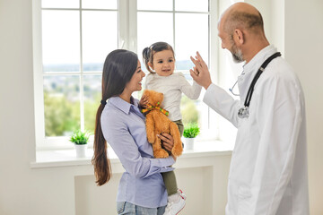 Family doctor.Senior doctor giving high five to girl at medical office. Little patient with her...