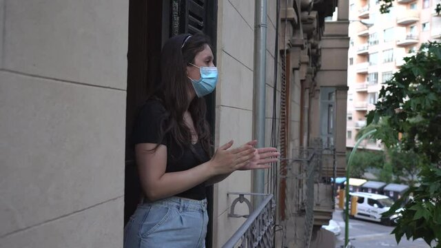 Young Spanish woman applauding from the balcony of her apartment as a sign of the Spanish health services against Covid 19