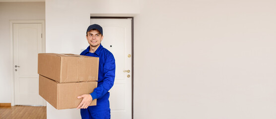 Fototapeta na wymiar Young happy delivery man in blue uniform is shipping a parcel for the client.