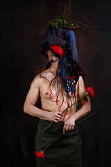Art project with a person whose headdress is made of fabric, moss and branches. A man holds two roses in his hands