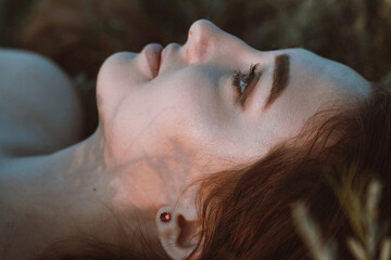 Naklejka premium close-up face of beautiful girl lying on the grass , young woman with long hair on nature,summer tender photo in village