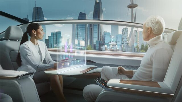 Casual Business Meeting Between Senior Male and Female inside a Futuristic Driverless Autonomous Car with Augmented Reality Presentation Interface. Self-Driving Van Driving on Downtown City Streets. 