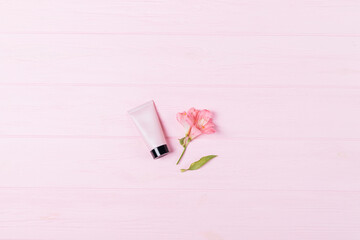Small tube of face cream next to delicate pink flower bud