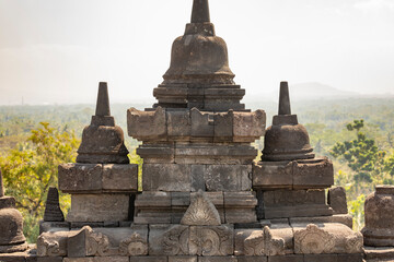 Details of various stupas that crown the balustrades and walls of the different levels of the Borobudur temple in Central Java, Indonesia, in the background, shreds of the surrounding landscape.