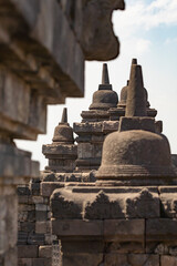 Details of various stupas that crown the balustrades and walls of the different levels of the Borobudur temple in Central Java, Indonesia, in the background, shreds of the surrounding landscape.