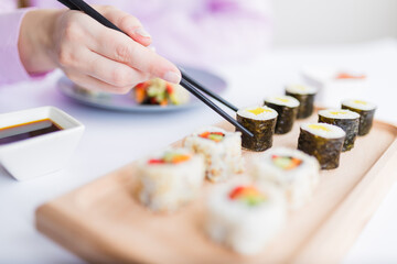 Close up of female eating sushi portion roll with chopsticks at restaurant.