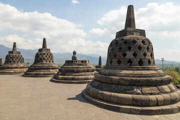 Top of the empty Borobudur Buddhist temple in Central Java, Indonesia with its characteristic rhombus stupas on a hot, light-filled day.
