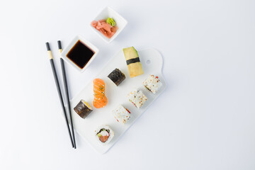 High angle view of sushi rolls and nigiri meal set with chopsticks, soy sauce, wasabi and gari on table.