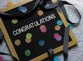 Congratulations word on a black desk with colourful round paper confetti, celebration phrase for winners, graduation and special occasions 