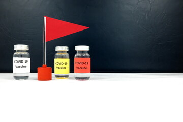 Multiple Covid-19 vaccine vials beside a red flag. Coronavirus vaccine candidate development race and competition concept.