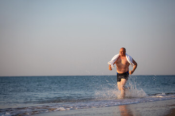 An elderly man runs along the beach.