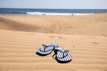 selective focus of striped flip flops on sand hills near Atlantic ocean against clear blue sky in Maspalomas, Gran Canaria
