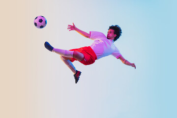 Kicking in jump, on the run. Football or soccer player on gradient background in neon light -...