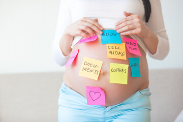 Young pregnant woman trying don`t forget stuff to hospital. Expecting female with notes on her...
