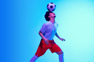 Fototapeta na wymiar Passioned for game. Football or soccer player on gradient blue studio background in neon light - motion, action, activity. Concept of sport, competition, winning, action, motion, overcoming. Copyspace
