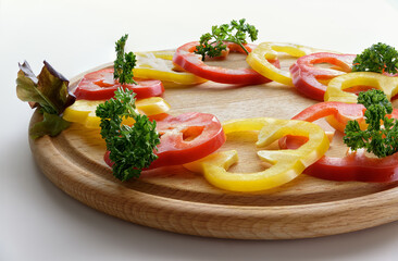 Raw Sliced Rad and yellow bell peppers composition with leaves of curly parsley on round wooden cutting board