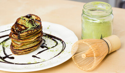 matcha banana pancakes on a light background with liquid chocolate next to green matcha powder and Bamboo Matcha Whisk. vegan food