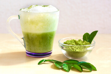 Horizontal shot of Green tea matcha latte with milk foam in a cup with green leaves and powed...