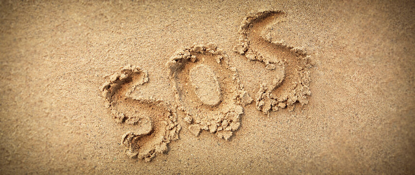 SOS on sand abbreviation written on a wide sandy background.