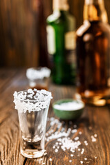An empty tequila glass, with salt at the edges, stands on the bar, in the background are different bottles of alcohol, shallow depth of field, selective focus. The concept of a drink in the bar.