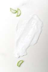 Vertical image.Top view of cream smear and aloe vera slices on the white marble surface
