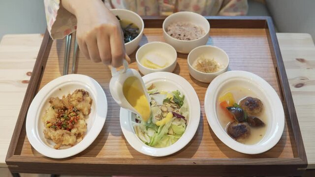 Woman spreading sauce on salad. Lunch at a room Served on tray at Korean postnatal hospital