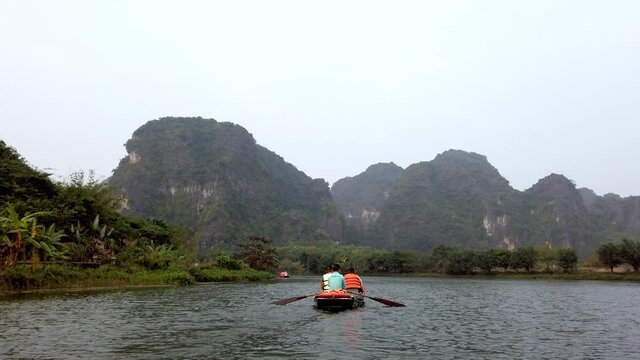Tour boat with tourists and guide paddling on Day River overlooking limestone Kerst mountain landscape, Handheld shot