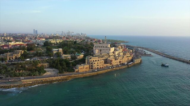 Aerial shot of church in city by sea against sky during sunset, drone flying forward towards buildings - Jaffa, Israel