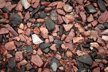 A closeup of wet textured rocks and stones of red, brown, orange and grey color