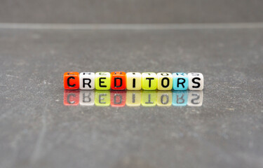 Conceptual of creditors, an item in balance sheet in audited financial accounts spelled on colorful alphabet beads. Isolated over reflective dark background. Focus on beads; other in gradient blur.