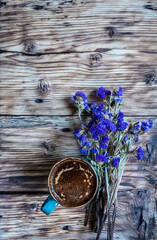 Cup of coffee and  bouquet of blue flowers on wooden rustic background, with copy space