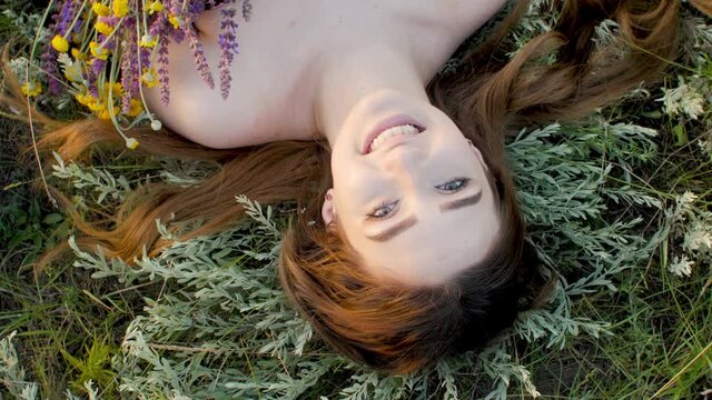 close-up face of beautiful girl lying on the grass with bouquet of wildflowers, young woman with long hair on nature