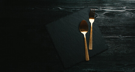 menu design, black wooden background with a golden spoon and fork