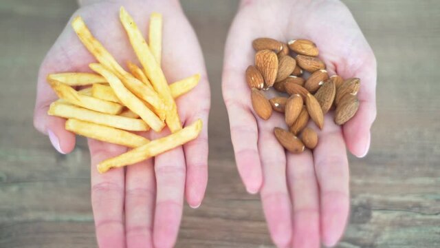 Choosing healthy or harmful food. Almond nuts or French fries in hands