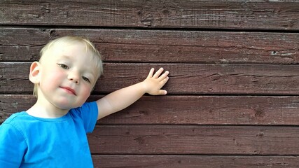 little smiling boy in a bright blue t-shirt shows something on the background of a brown wooden...