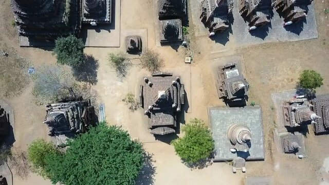 Aerial top view of Buddhist temples amidst plants on sunny day, drone ascending over pagodas - Bagan, Myanmar